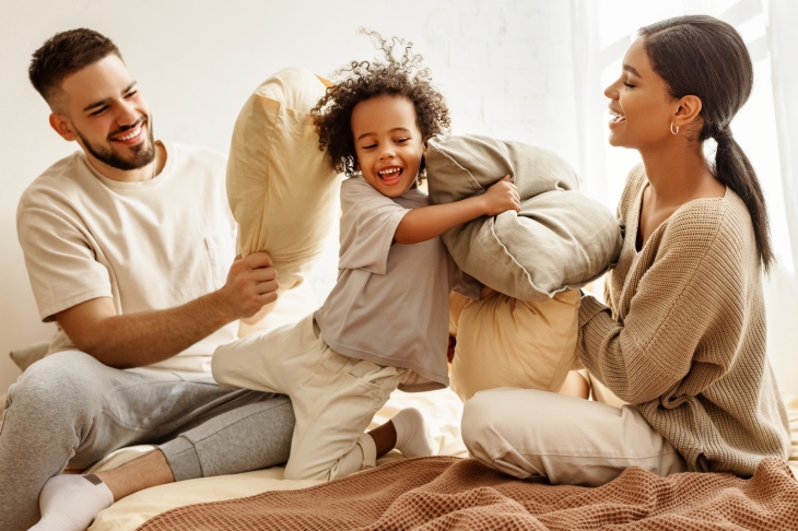 happy family multiethnic mother, father and son  laughing, playing, fights pillows and jumping in bed in bedroom at home